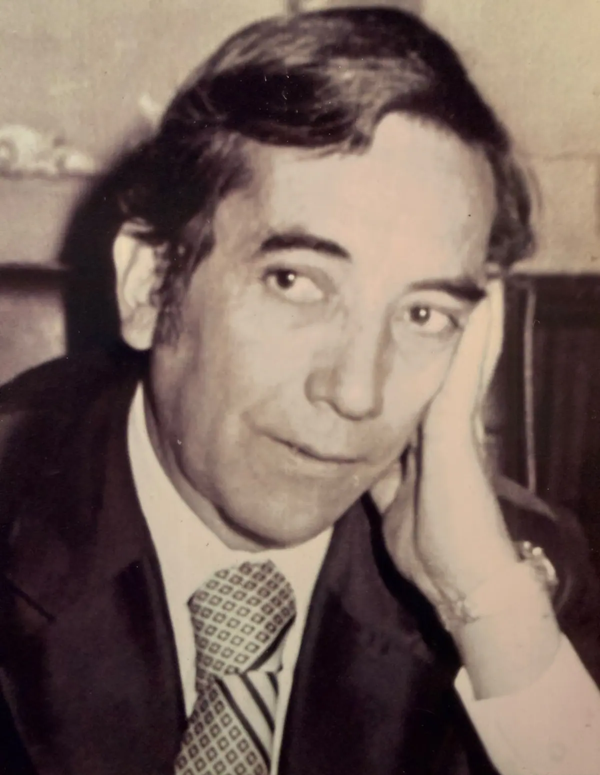 Vintage portrait of Mike Gallegos in a suit and tie, resting his cheek on his hand