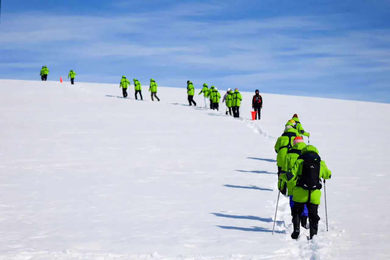A line of travelers in expedition jackets crossing an Antarctic snowfield
