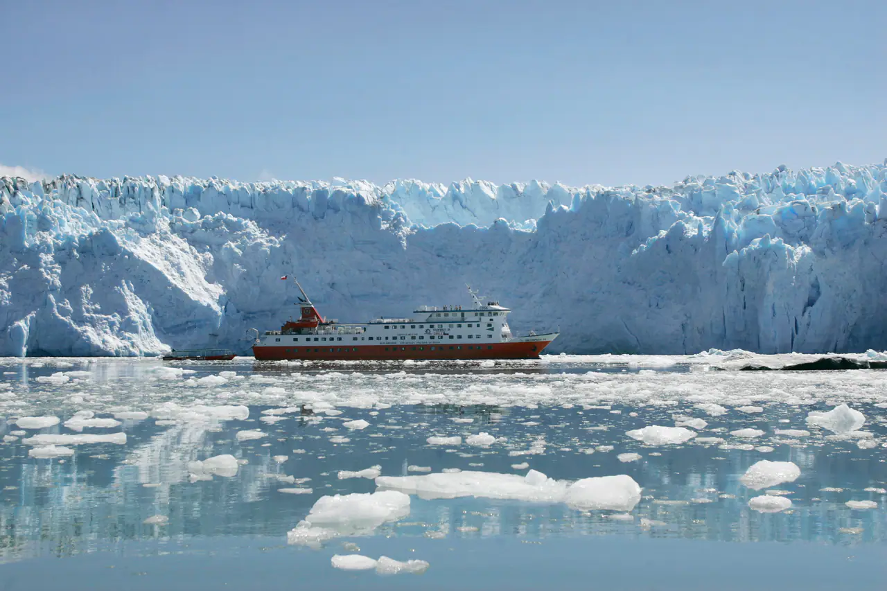 An expedition ship anchored before a glacier among floating ice