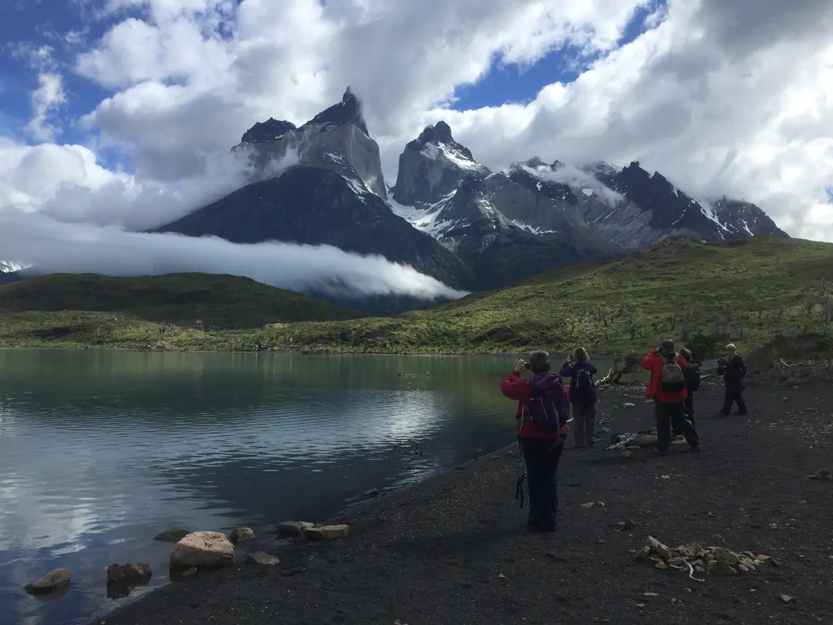 A group walking along a lakeshore below the Cuernos del Paine