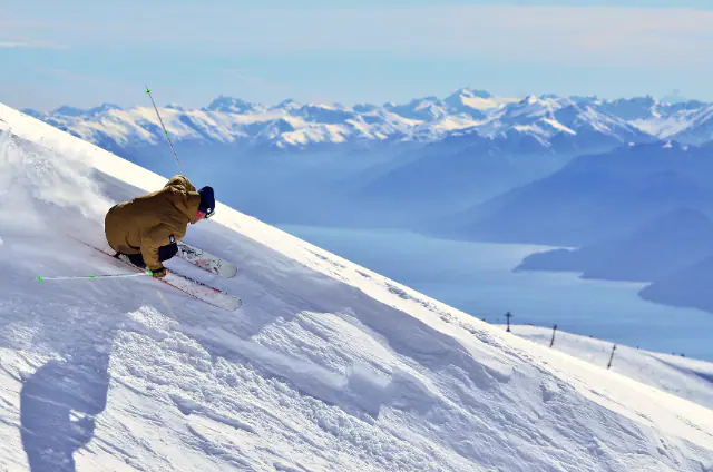 A skier carving down an Andean slope above a lake